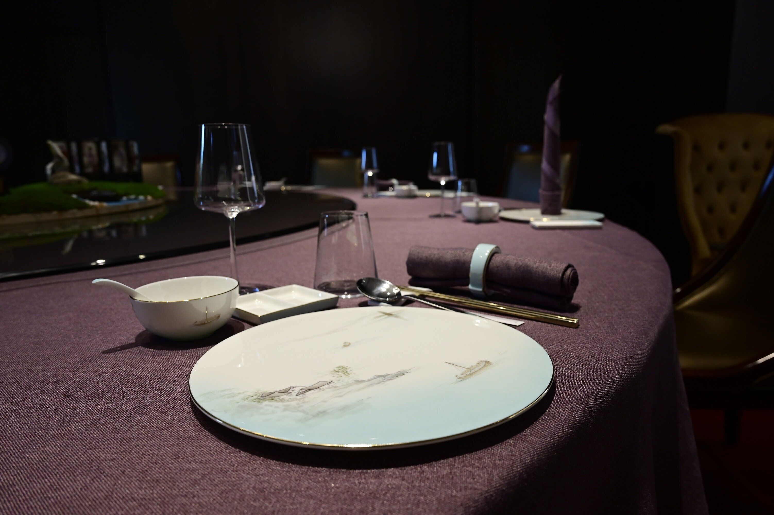 Een eettafel gedekt met een bord, kom, lepel en wijnglas.