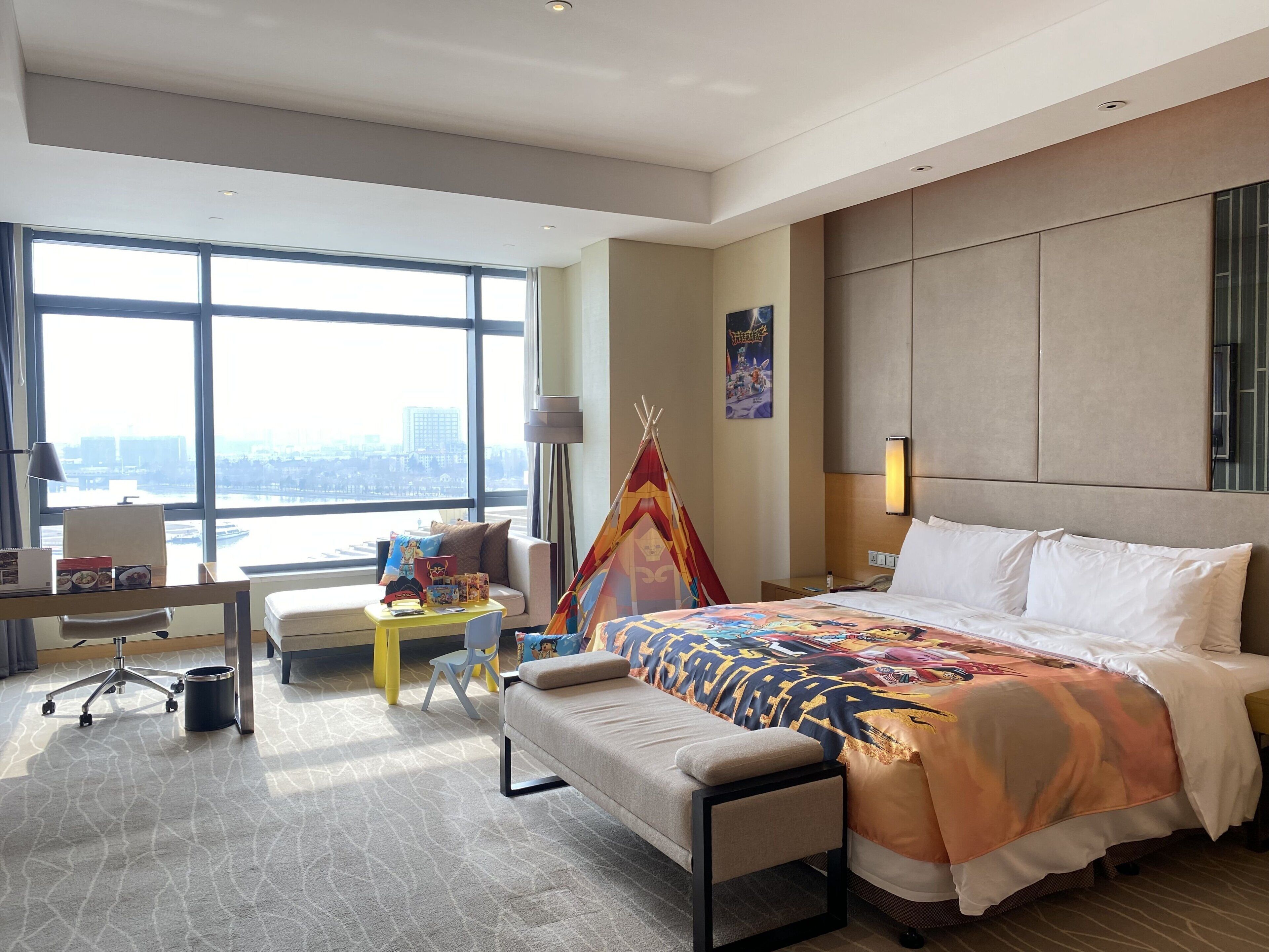 A hotel room with a large bed, a desk, a chair, and a view of the city.