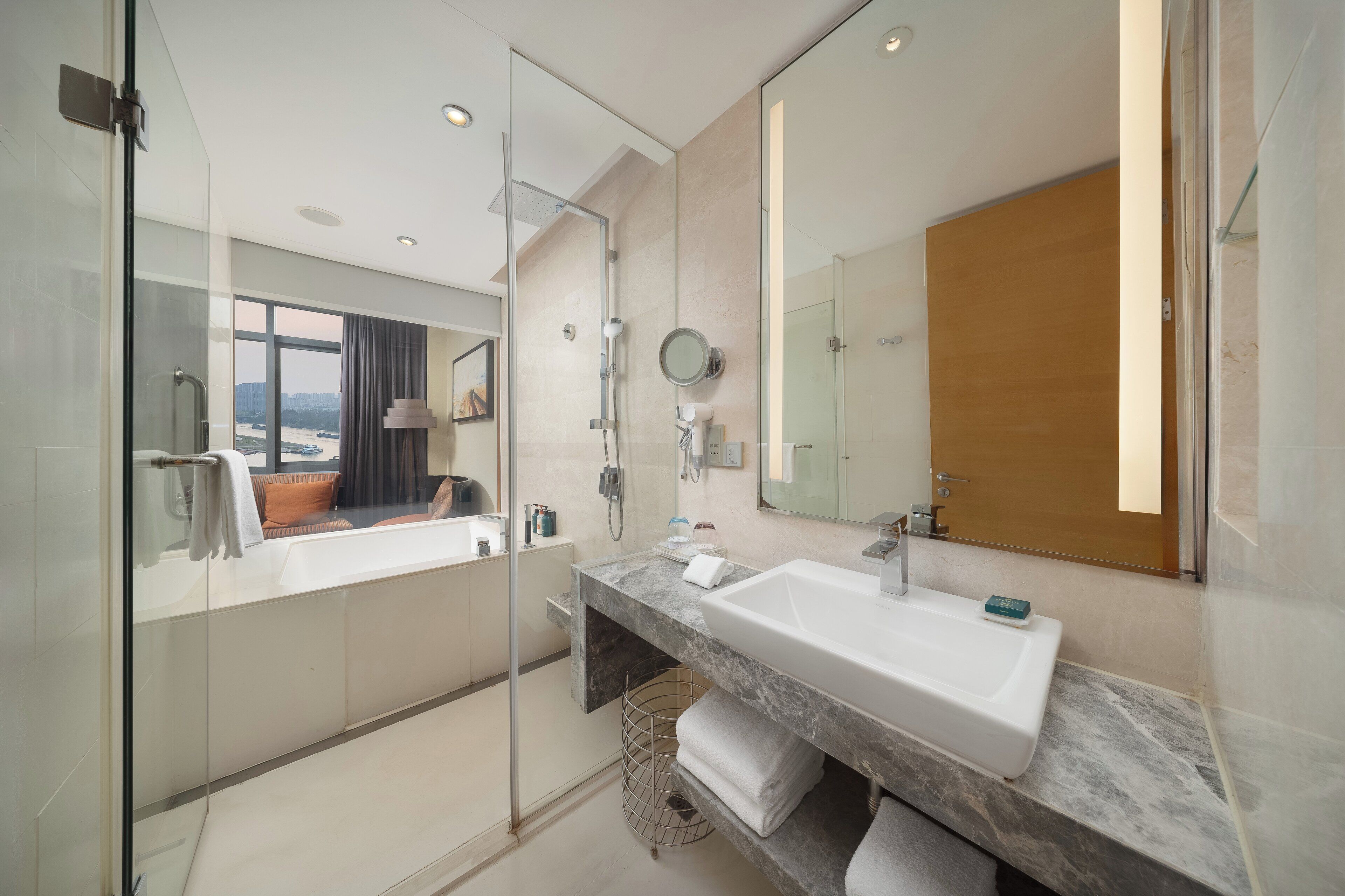 A modern bathroom with a glass-enclosed shower, a large mirror, and a marble countertop.