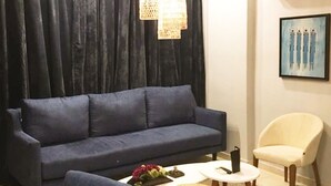 Een moderne woonkamer met een donkerblauwe bank, een witte salontafel, een rieten krukje en een roomkleurige fauteuil.