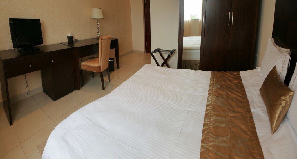 Una habitación de hotel con una cama, un escritorio con computadora, una silla y un armario.