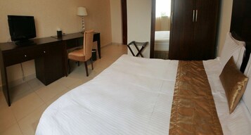 Una habitación de hotel con una cama, un escritorio con computadora, una silla y un armario.
