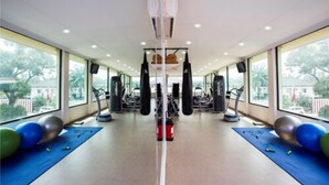 Een sportschool met trainingsapparatuur, grote ramen en fitnessmatten.