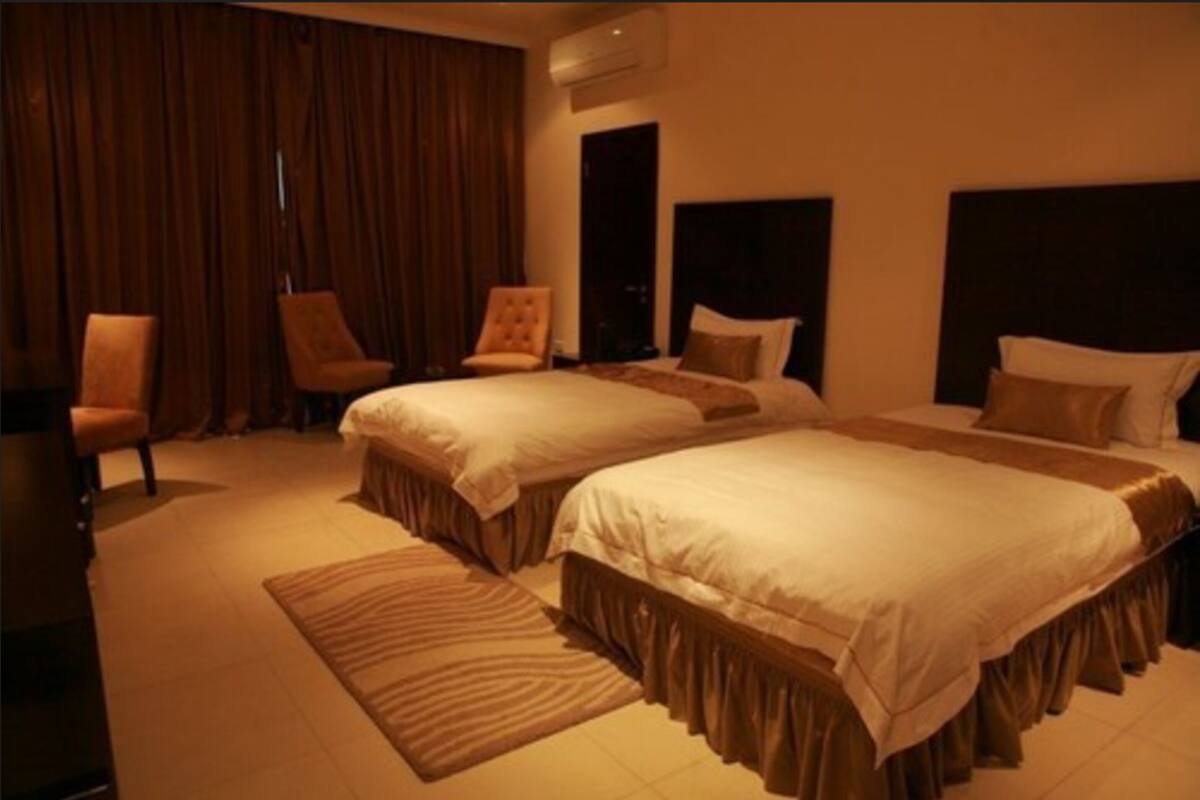 A hotel room with two beds, a large window with curtains, a chair, and a rug.