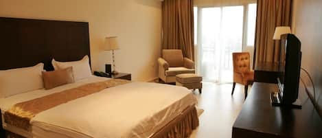 A hotel room with a large bed, a desk with a television, a chair, and a window with curtains.