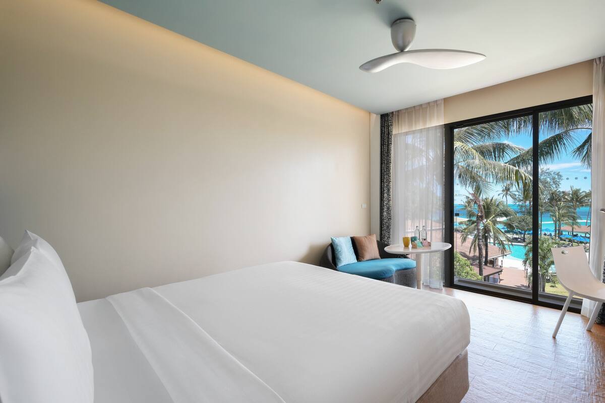 Habitación de hotel con una cama grande, una mesita pequeña y vistas a una piscina y palmeras.
