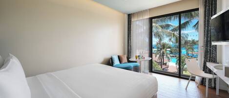 A hotel room with a bed, a desk, a chair, and a view of a pool and palm trees.