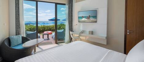 A hotel room with a bed, a desk, a chair, a sofa, a TV, and a view of the ocean.