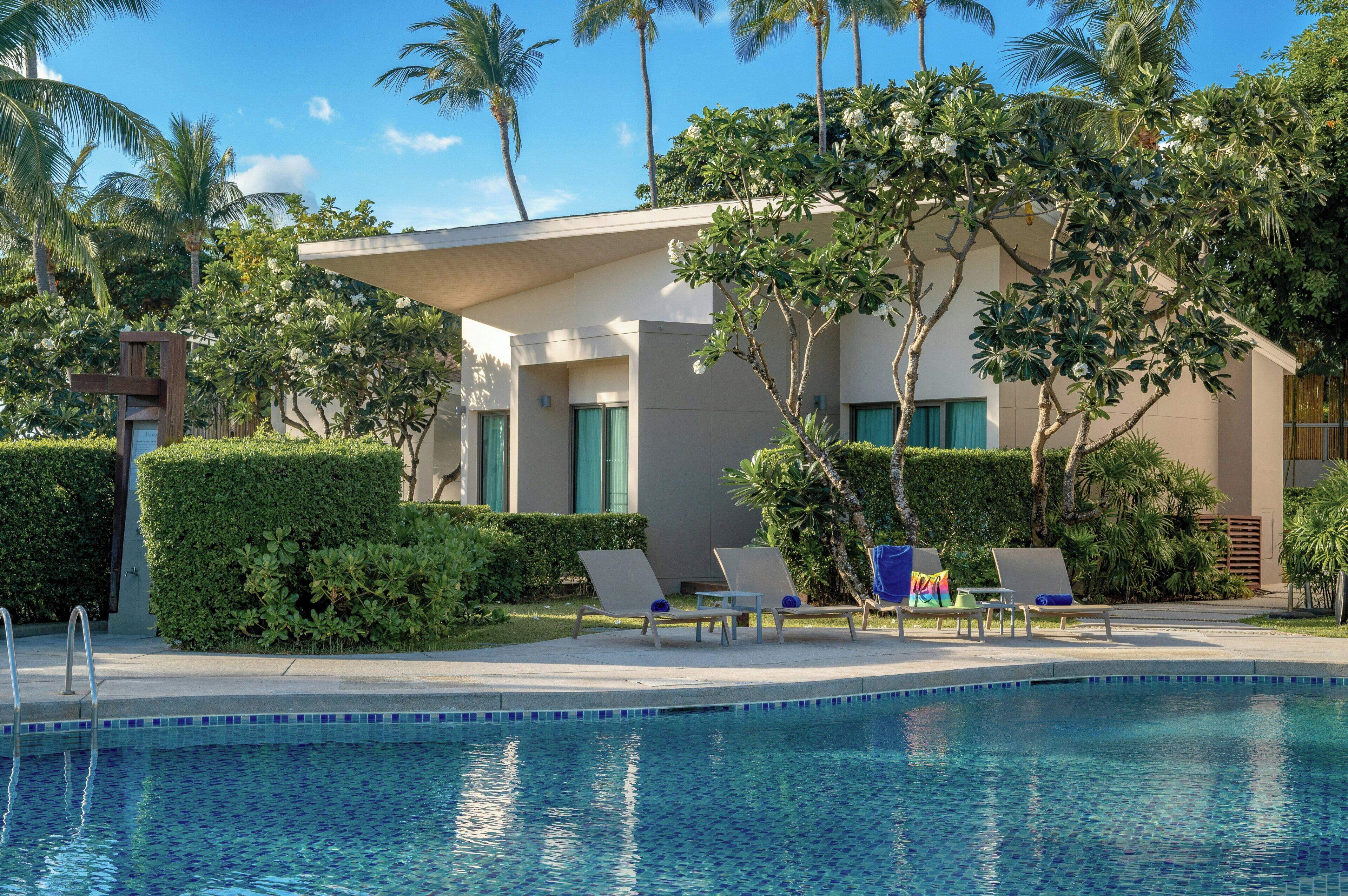 A pool area with lounge chairs, a modern building, and tropical vegetation.