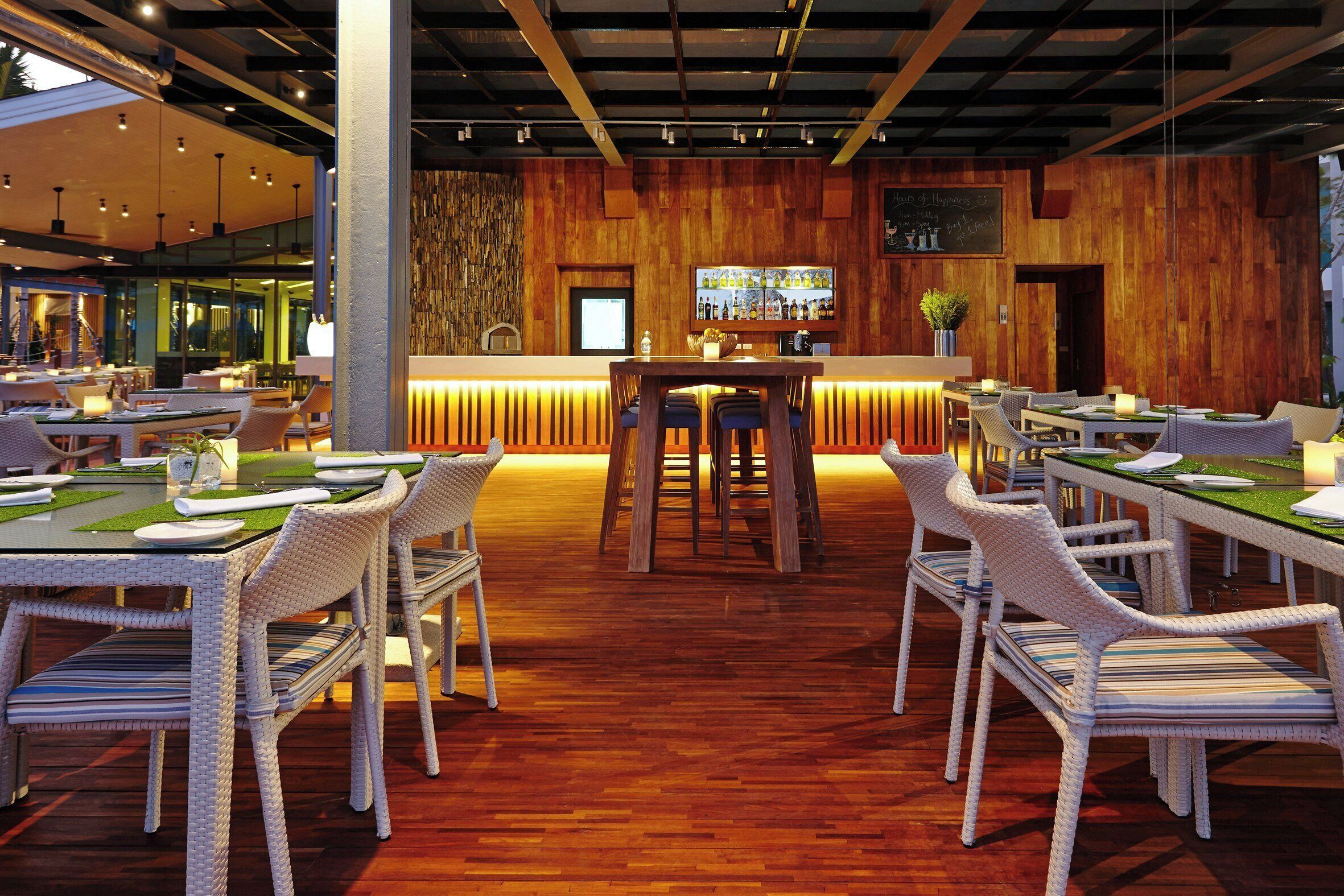 Un restaurante con mobiliario de mimbre, una zona de bar y una pared de madera con un televisor.