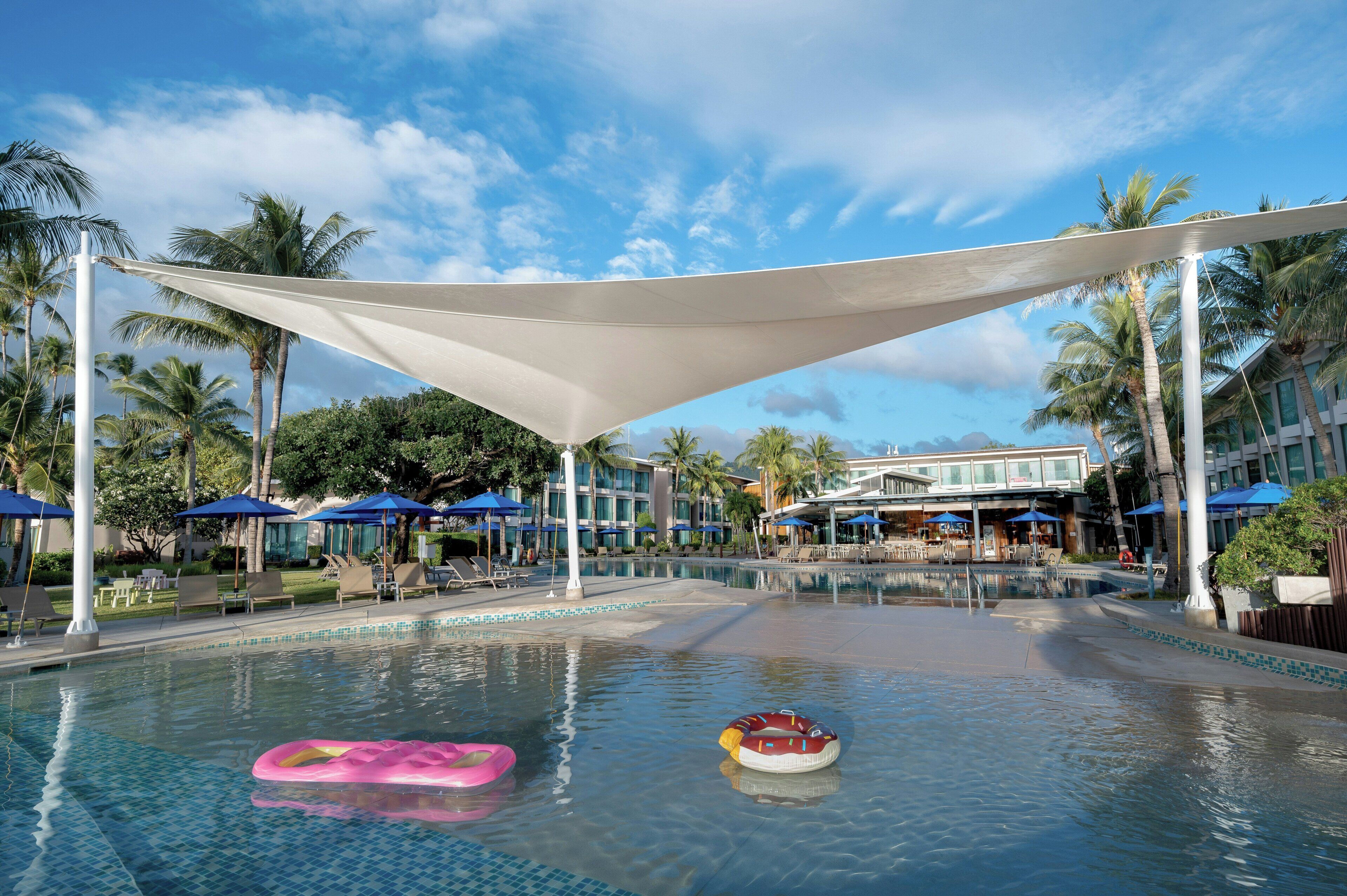 A pool area with lounge chairs, umbrellas, and palm trees.