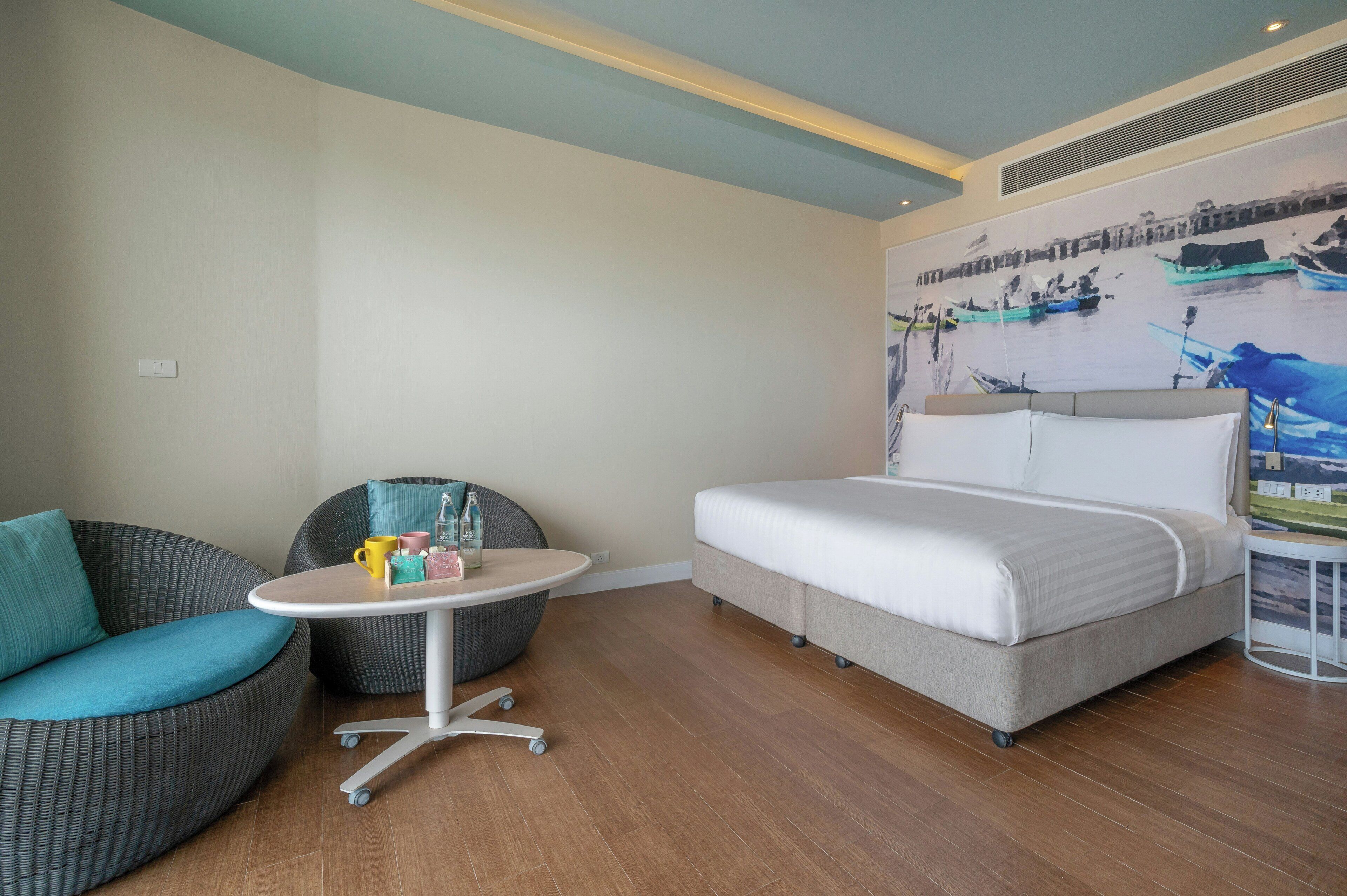 A hotel room with a bed, a round table with chairs, a sofa, and a mural on the wall.