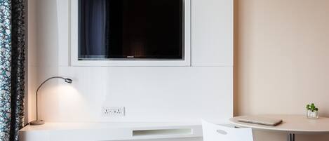 A modern, minimalist room with a built-in desk, a flat-screen TV, a desk lamp, and a small table with a plant.