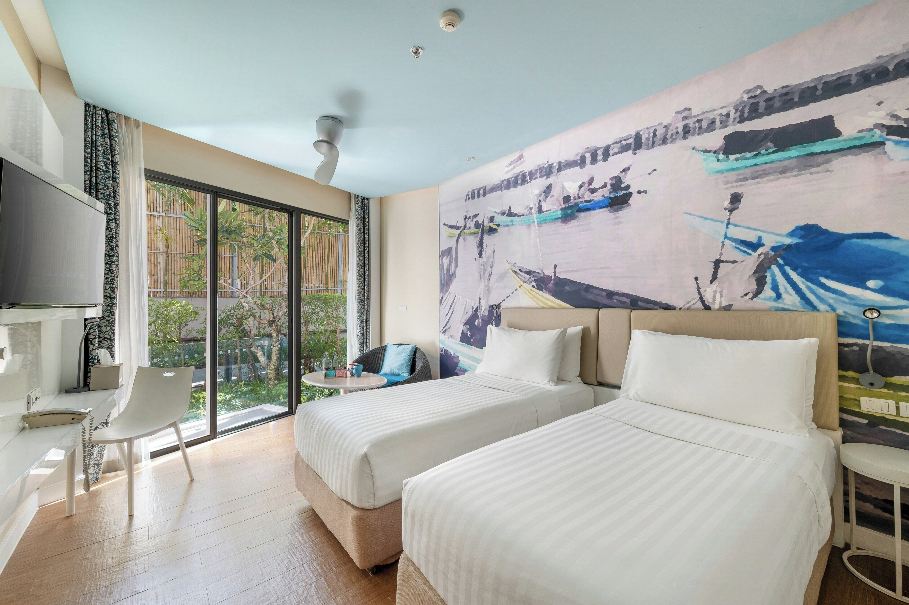 A hotel room with two beds, a desk, a chair, a TV, and a large window with a view of greenery.
