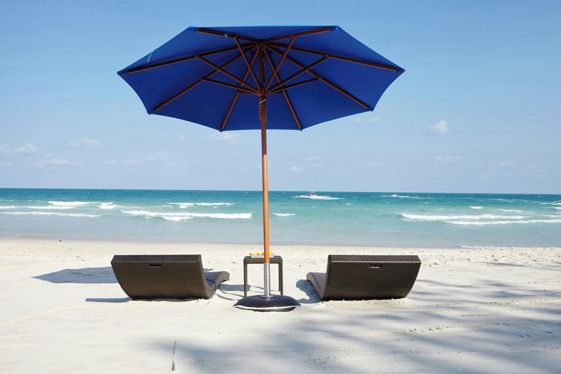 A beach umbrella, two wicker chairs, and a sandy beach with ocean waves in the background.
