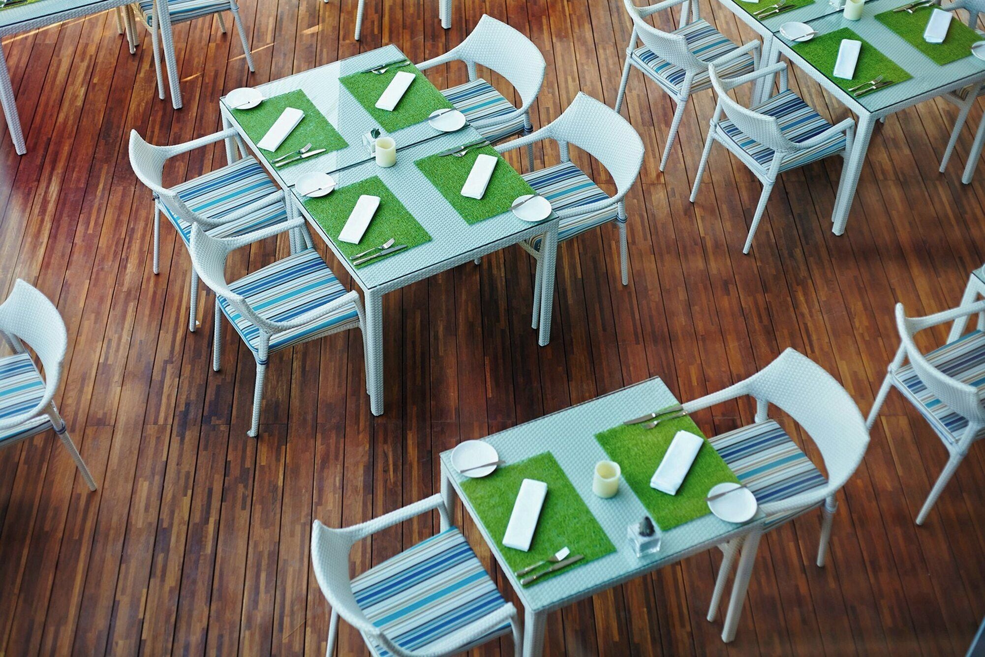 A dining area with multiple tables and chairs, each set with white plates, silverware, and green placemats.