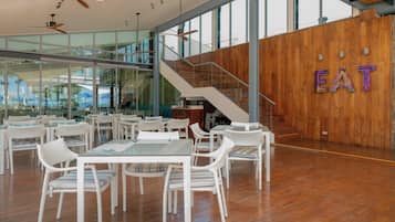 Un comedor moderno con mobiliario de mimbre blanco, una pared de madera con un letrero y una escalera.
