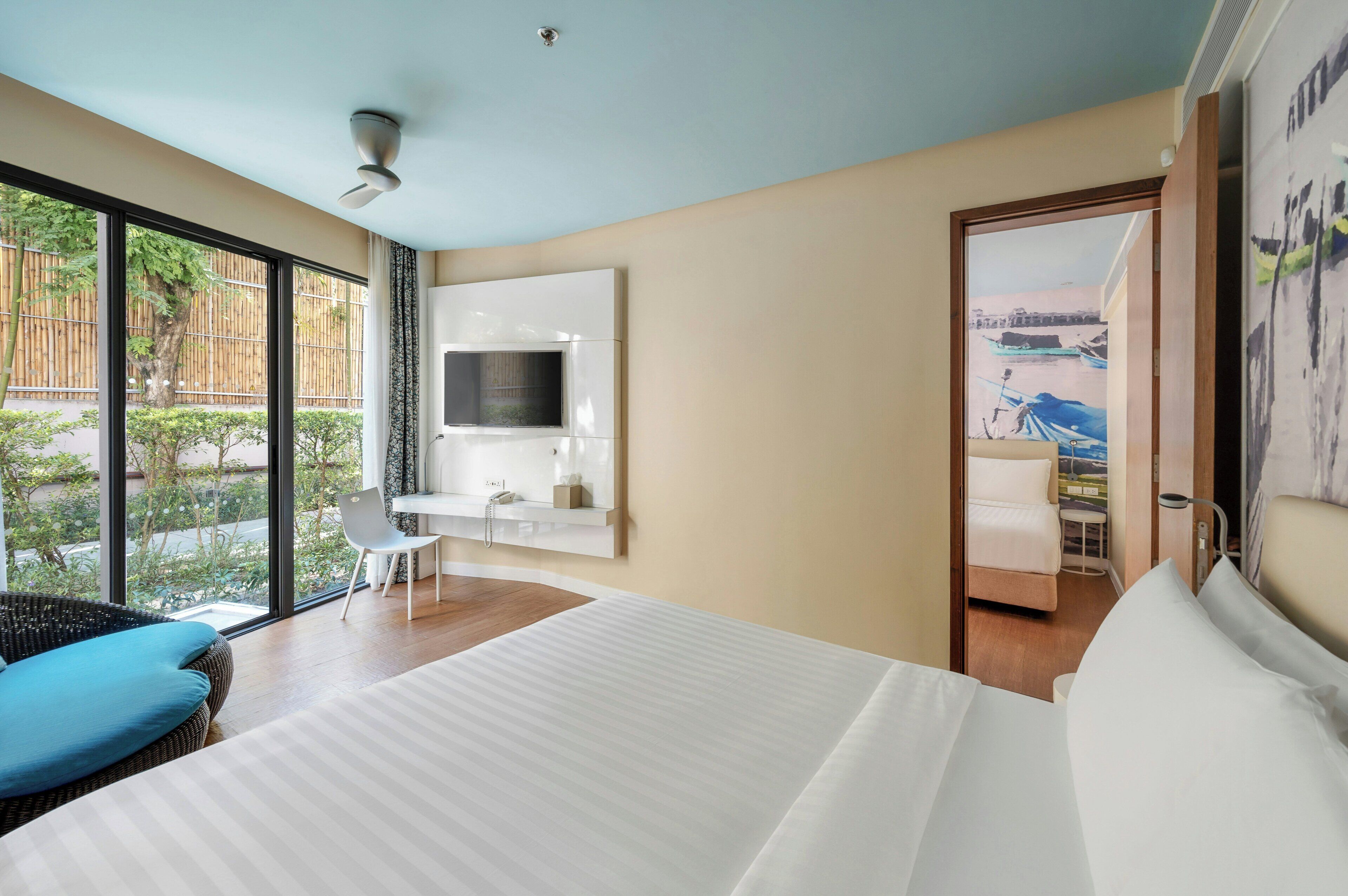 Habitación de hotel con cama, escritorio, silla, televisor y vistas al exterior.