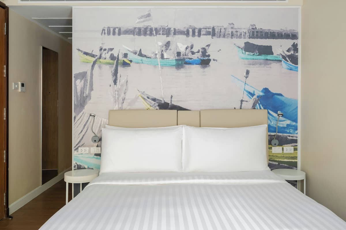 Una habitación de hotel con una cama, una mesita de noche, una lámpara de pared y un cuadro de barcos en un río.