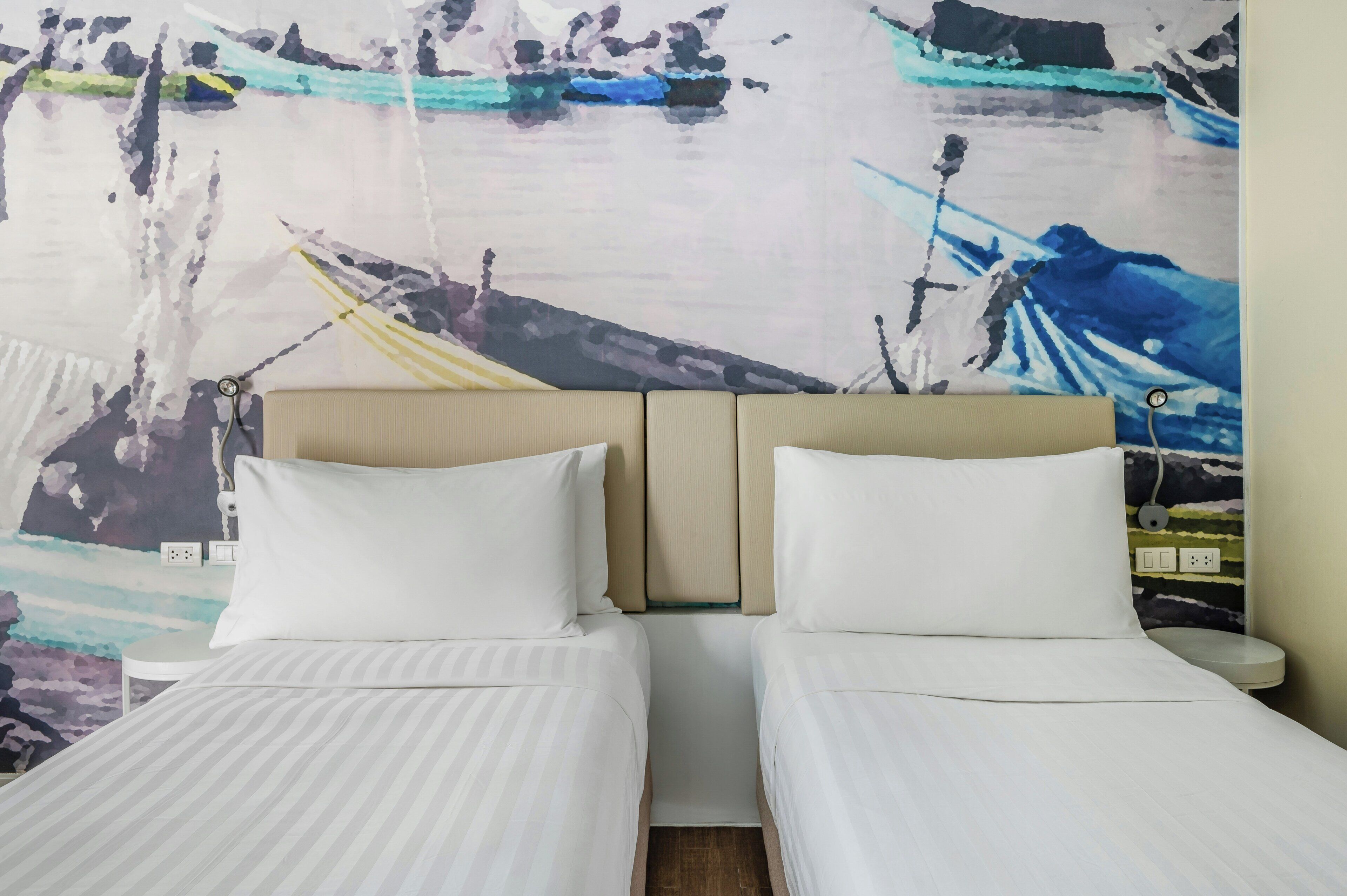 A hotel room with two beds, a headboard, a nightstand, and a wall with a nautical-themed mural.