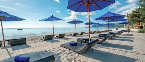 A beach with lounge chairs and blue umbrellas.