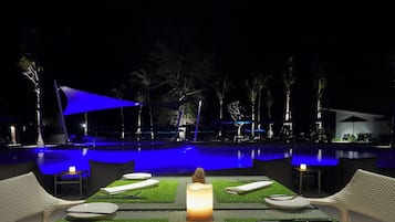 A nighttime pool area with lounge chairs, a table with a candle, and a blue canopy.