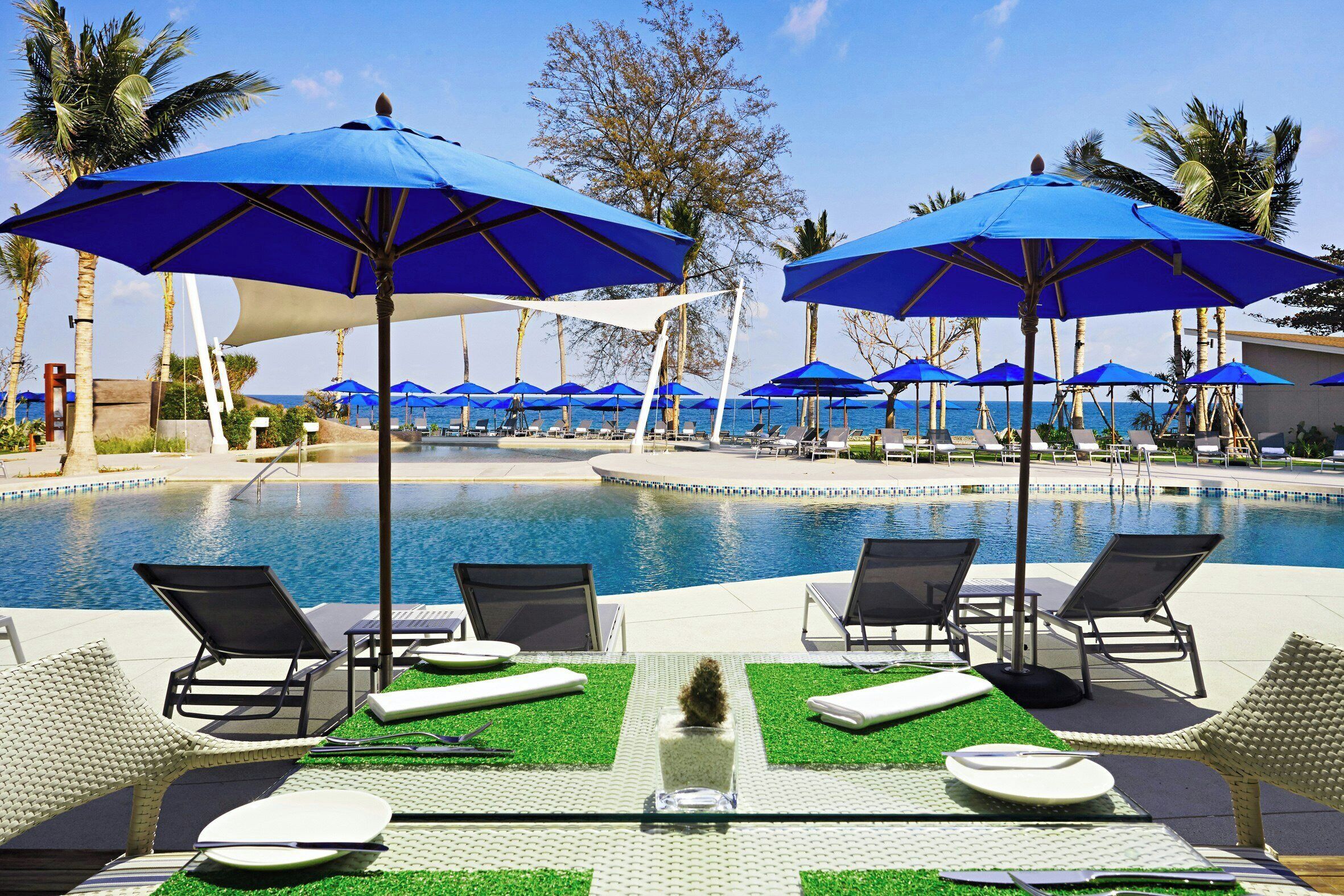 A poolside area with lounge chairs, blue umbrellas, and a clear view of the pool.