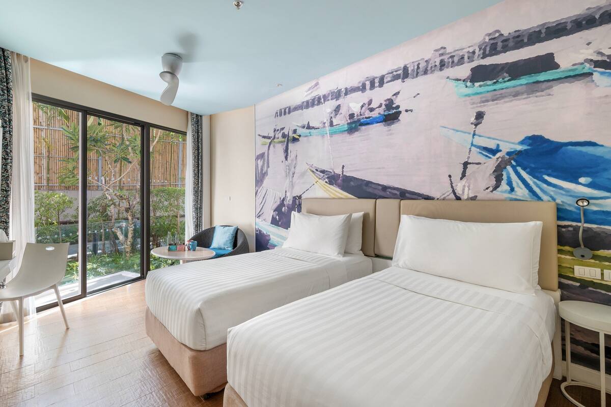 Habitación de hotel con dos camas, un ventanal con vistas a zonas verdes y un cuadro en la pared.