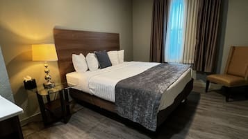 A hotel room with a large bed, a bedside table with a lamp, a chair, and a view of the outdoors through the window.