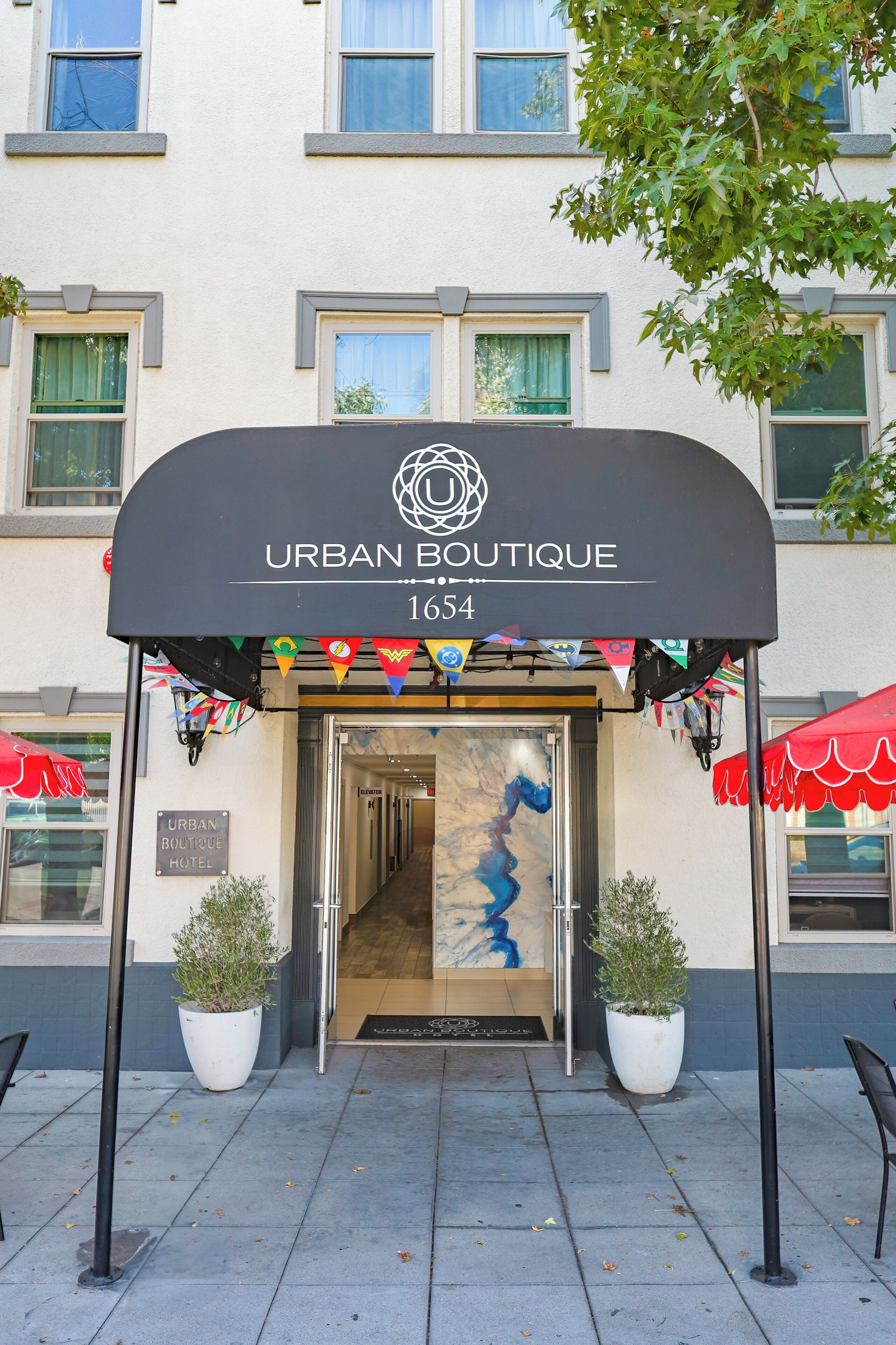 L’entrée de l’hôtel Urban Boutique, dotée d’un design moderne, se distingue par une grande porte vitrée et un auvent noir.