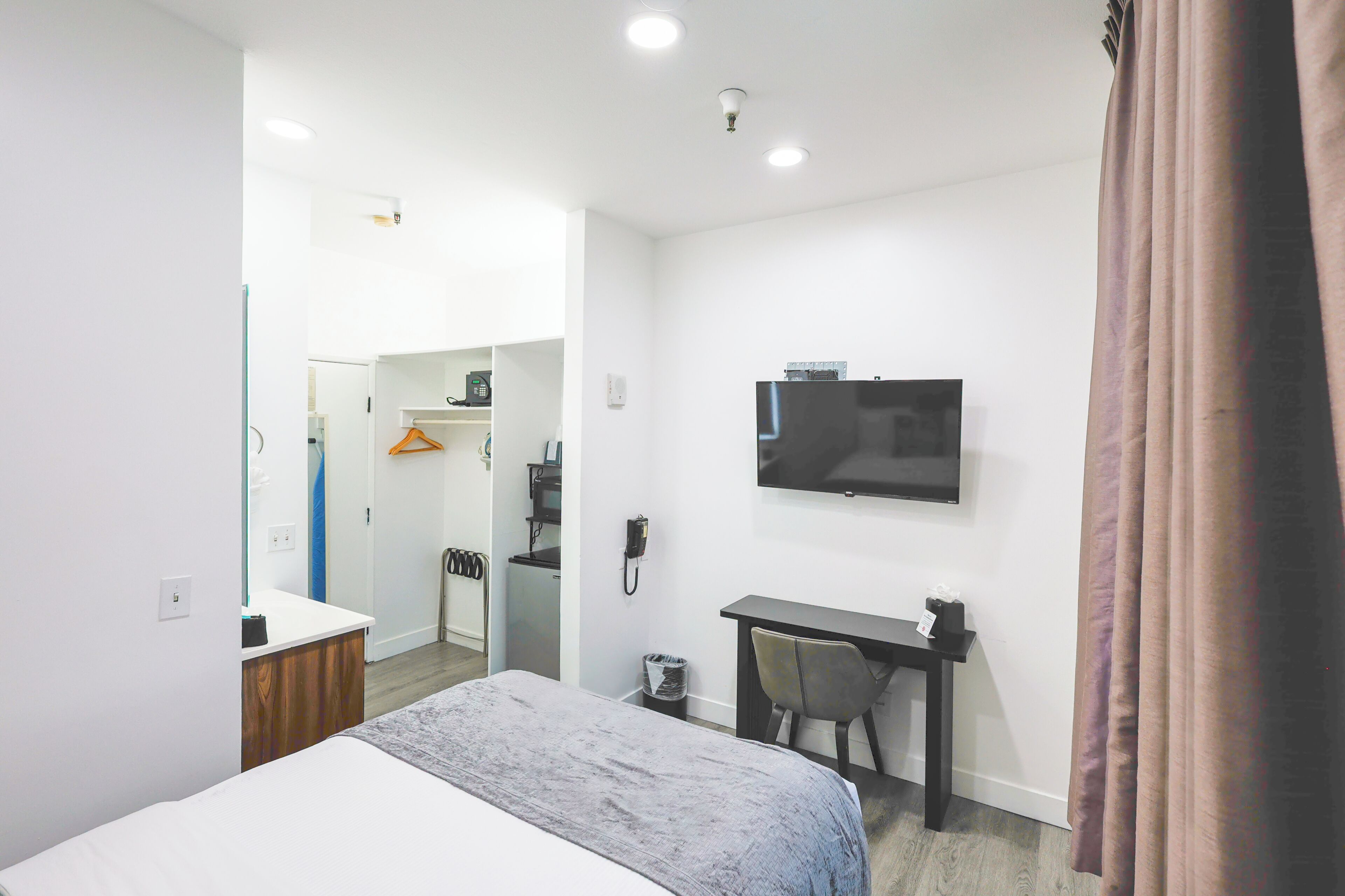 A hotel room with a bed, desk, chair, television, and a bathroom visible through an open door.