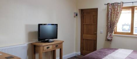 A hotel room with a bed, a TV on a wooden stand, a door, and a window with curtains.