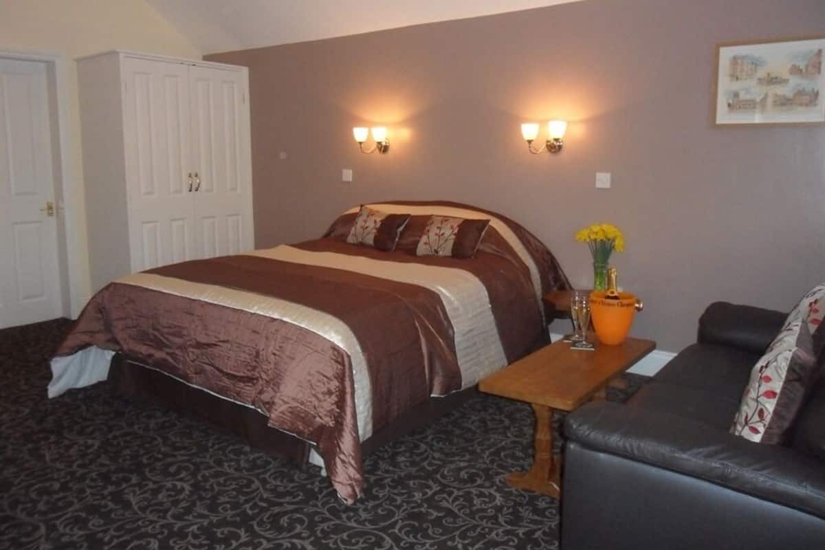 Quarto com cama grande, mesa de cabeceira de madeira, uma cadeira e duas luminárias fixadas na parede.