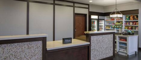 A hotel reception area with a tiled mosaic wall, a reception desk, and a self-service kiosk.