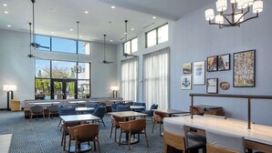 A spacious hotel lobby with multiple seating areas, large windows, ceiling fans, and artwork on the walls.