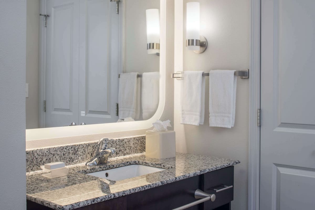 A bathroom with a granite countertop sink, a mirror, and two wall-mounted towel racks.
