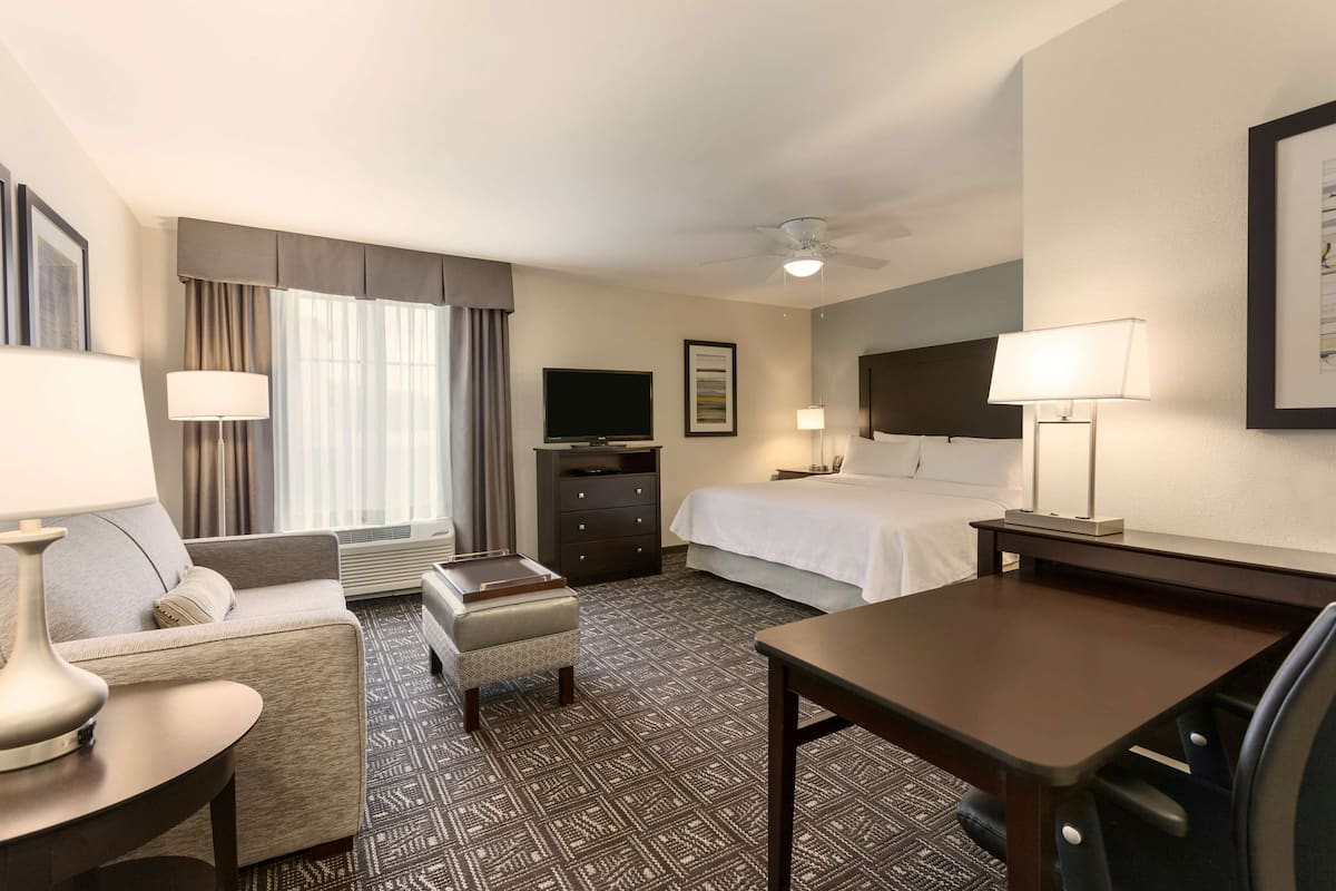 A hotel room with a bed, a desk, a chair, a TV, a lamp, and a window with curtains.