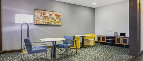 A hotel lobby with a gray wall, a painting, a reception desk, and seating with a patterned carpet.