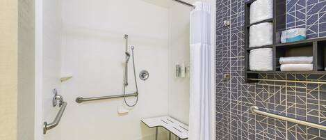 Un baño moderno con ducha a nivel, barras de apoyo, un asiento y un perchero para toallas.