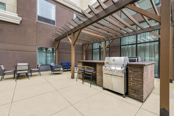 An outdoor patio with a grill, seating, and a pergola structure.