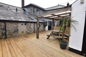 A wooden deck with a covered seating area, stone walls, and a potted plant.