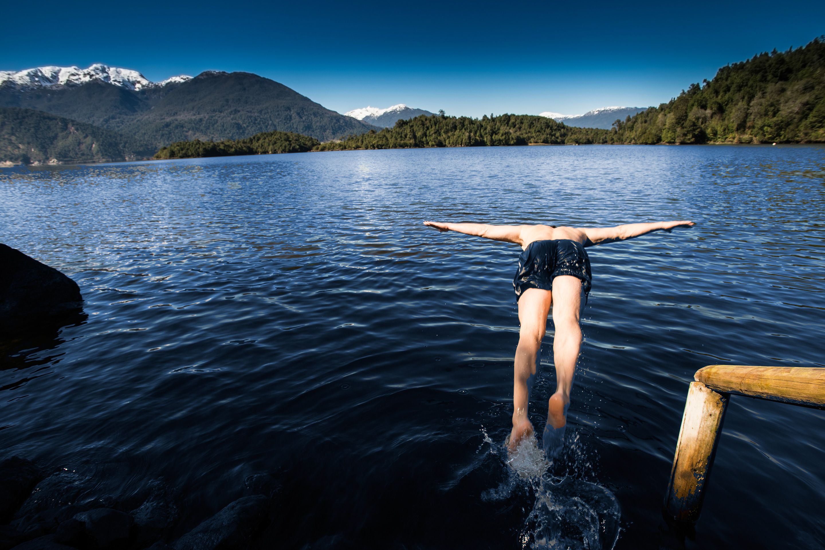 Una persona se sumerge en un lago con montañas al fondo.