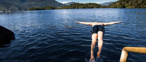 Una persona se sumerge en un lago con montañas al fondo.