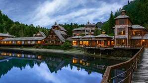 A lakeside lodge with multiple wooden cabins connected by a dock, surrounded by dense forest. - Puyuhuapi Lodge & Spa (Cisnes)