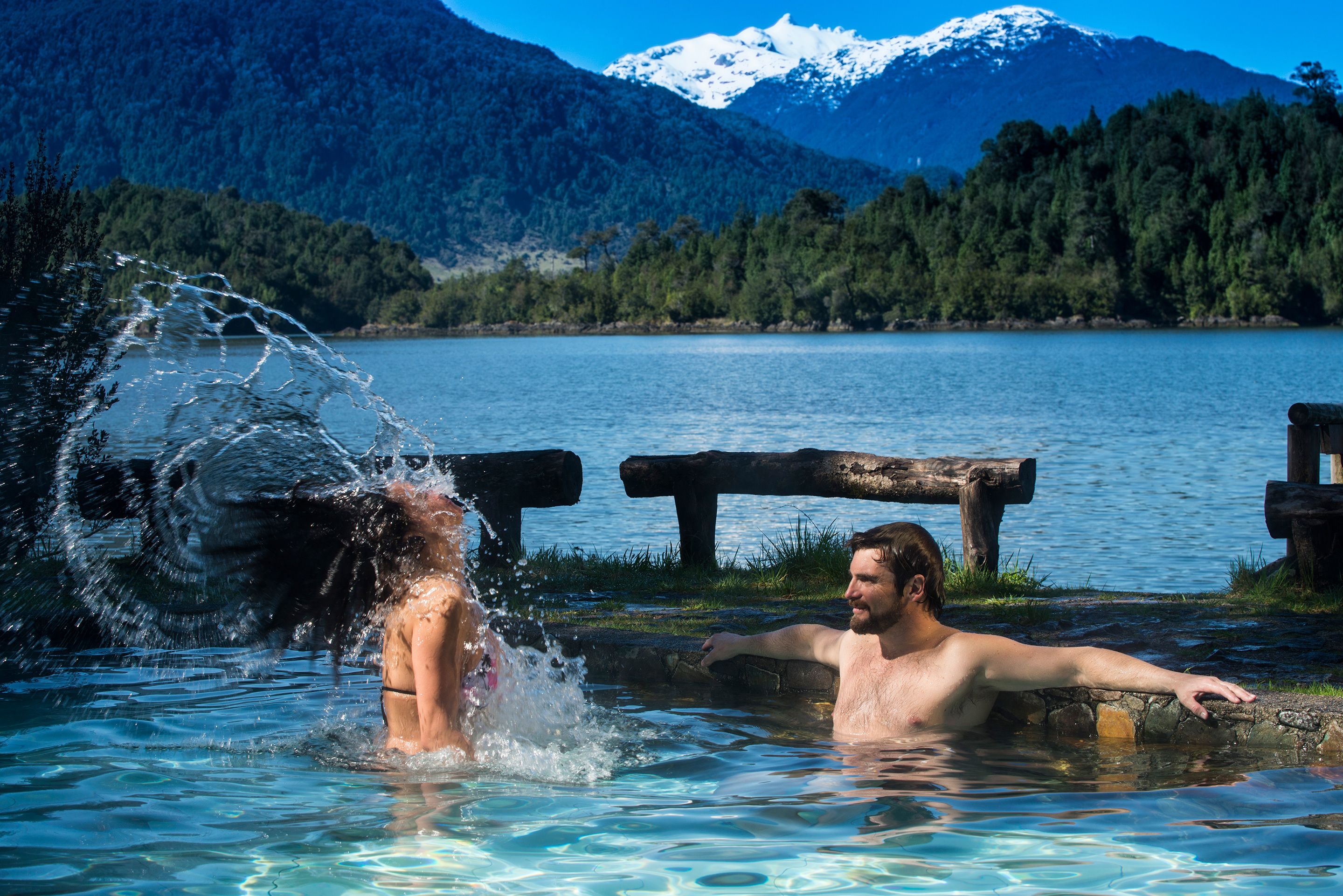 A man and a woman in a natural hot spring with a mountainous backdrop.