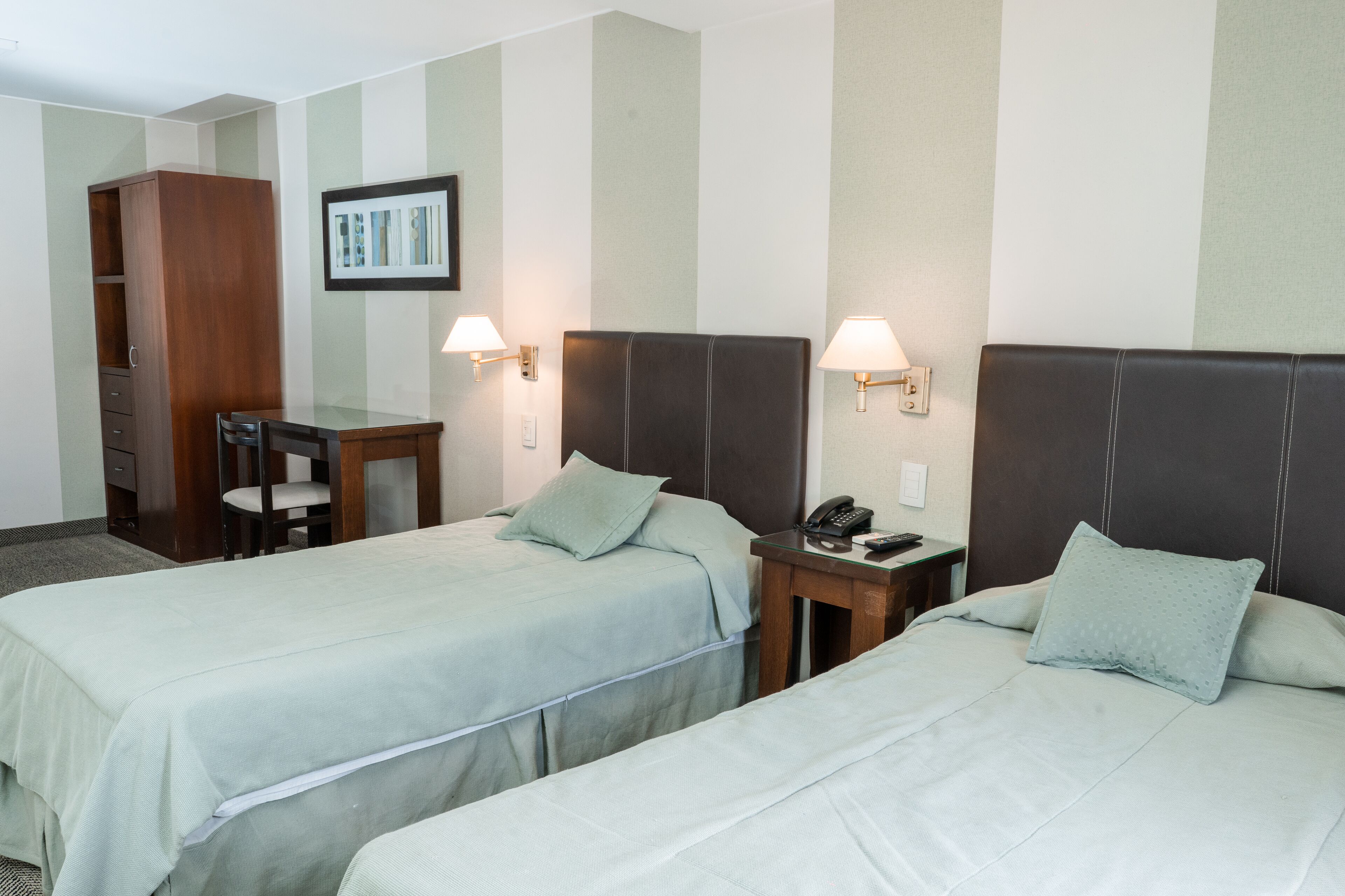 A hotel room with two single beds, a desk, a chair, a wardrobe, and a telephone.