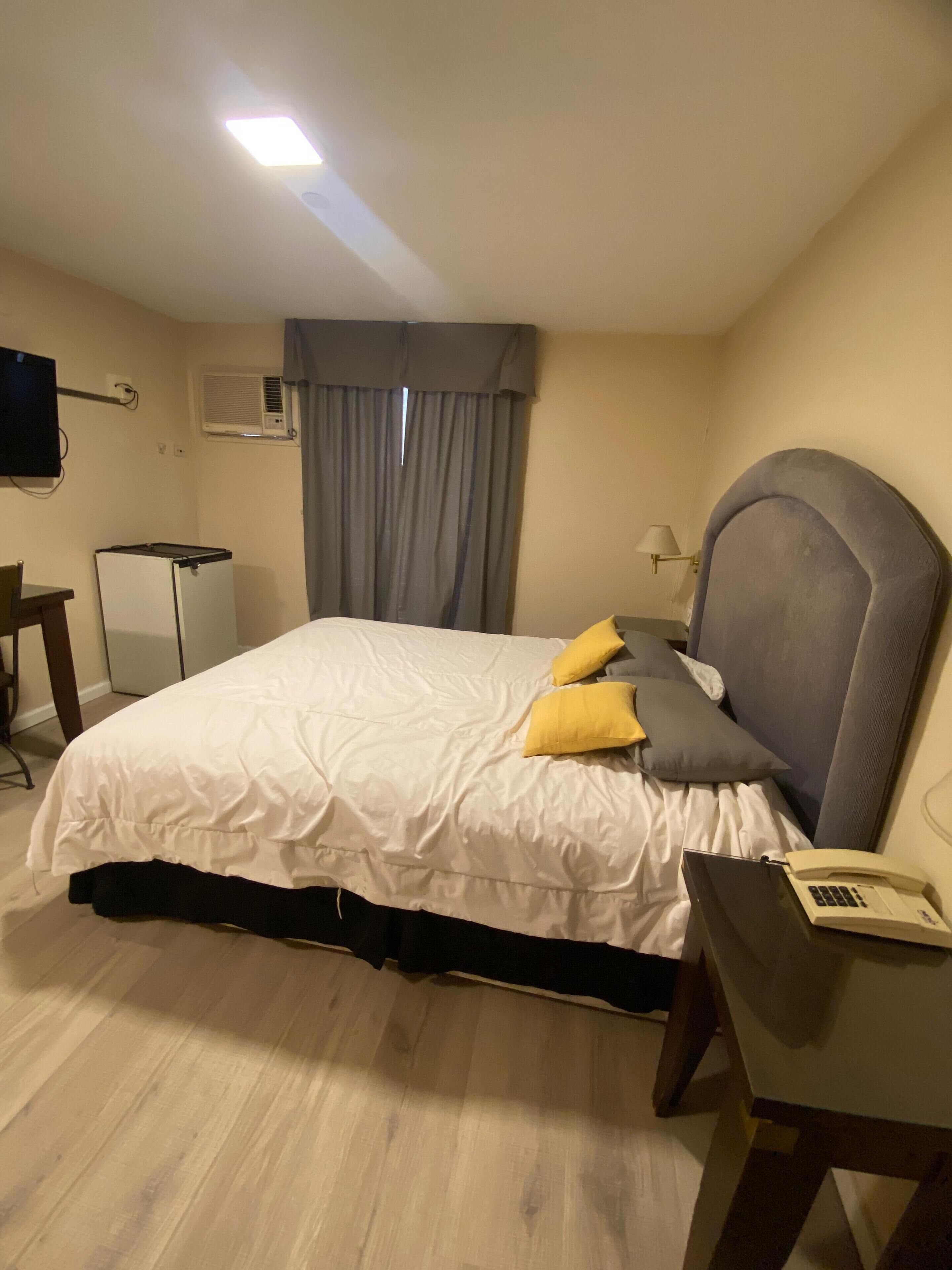 Quarto de hotel com cama, escrivaninha, cadeira, televisão e ar condicionado.