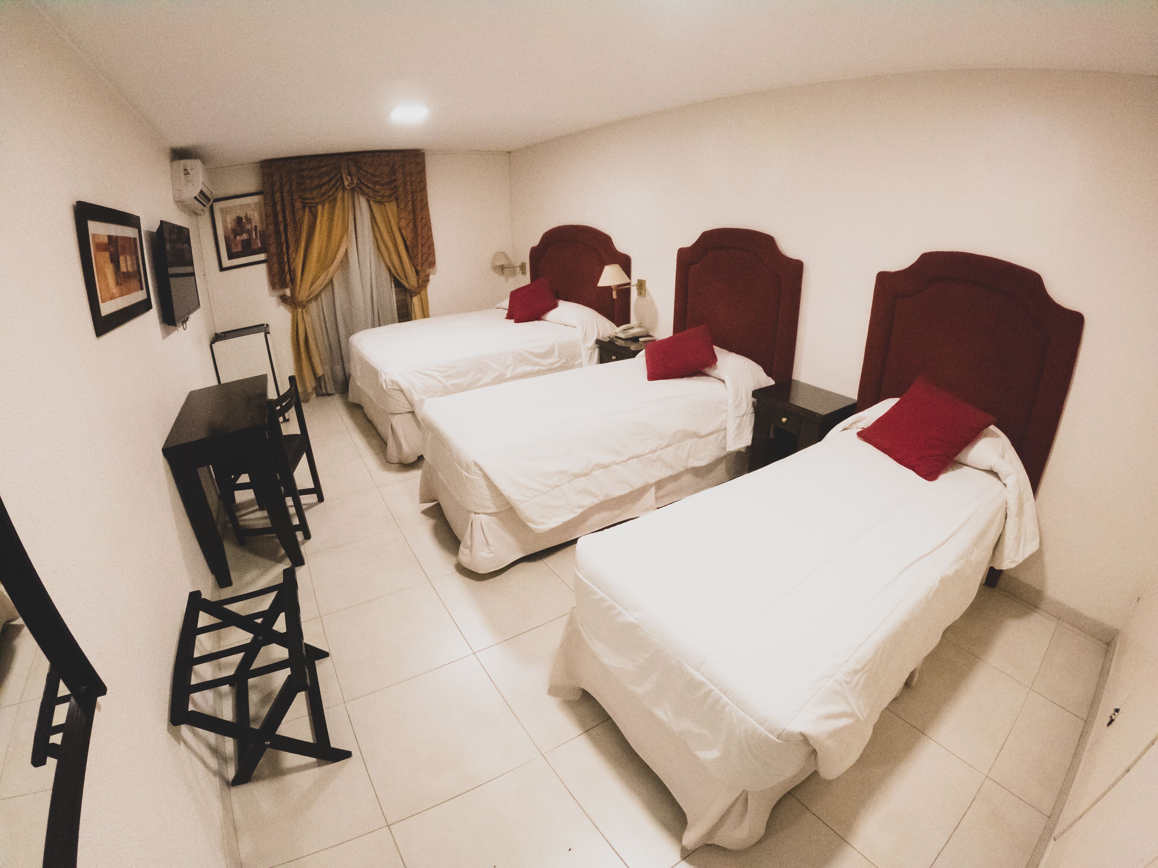 A hotel room with two single beds, a desk, a chair, and a small table.