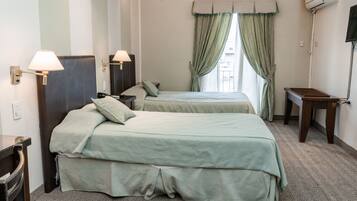 A hotel room with two beds, a desk, a chair, a lamp, and a window with curtains.