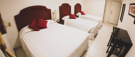 A hotel room with three beds, each with a red headboard and white bedding. There is a desk and a chair in the room.